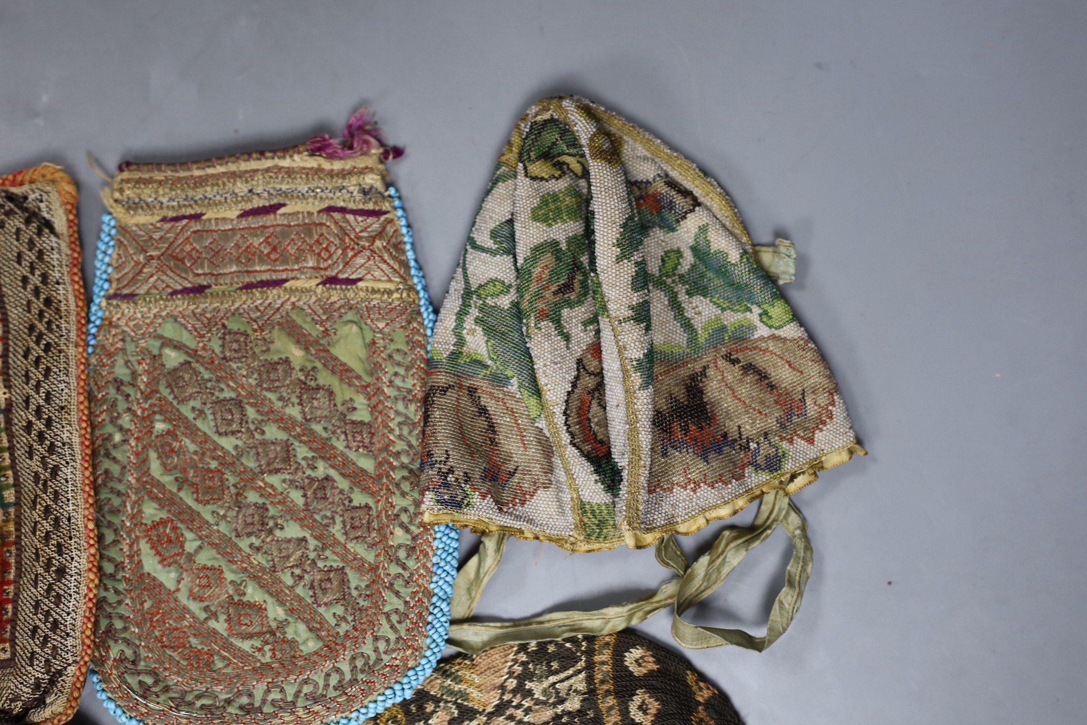 An early 19th century , possibly earlier, four sectioned floral bead worked reticule with ribbon handles, a hair and velvet pin cushion, a North African metallic embroidered bag, a similar bead and leather container, a k